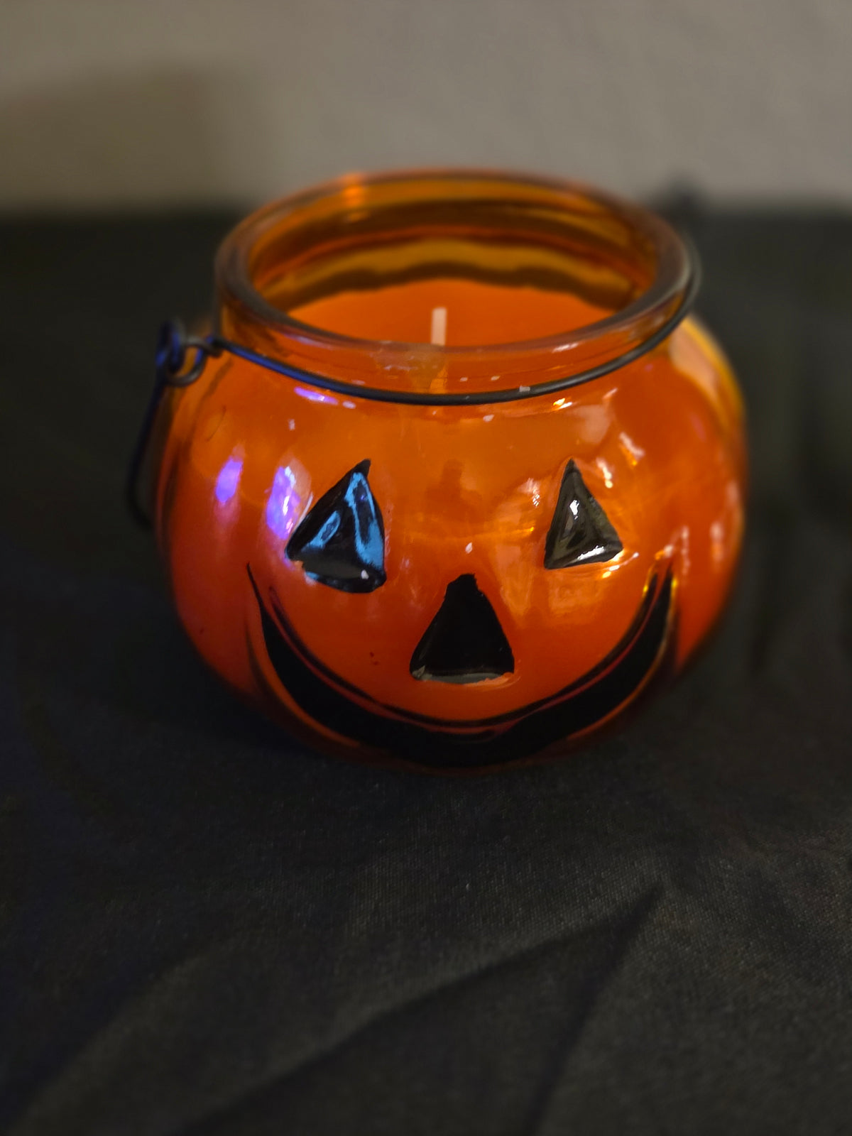 Candy corn-scented soy wax candle with orange wax in a glass jack-o’-lantern jar with a black wire handle.