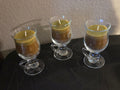 Three vanilla sage soy wax candles in clear footed glass mugs with curved handles.