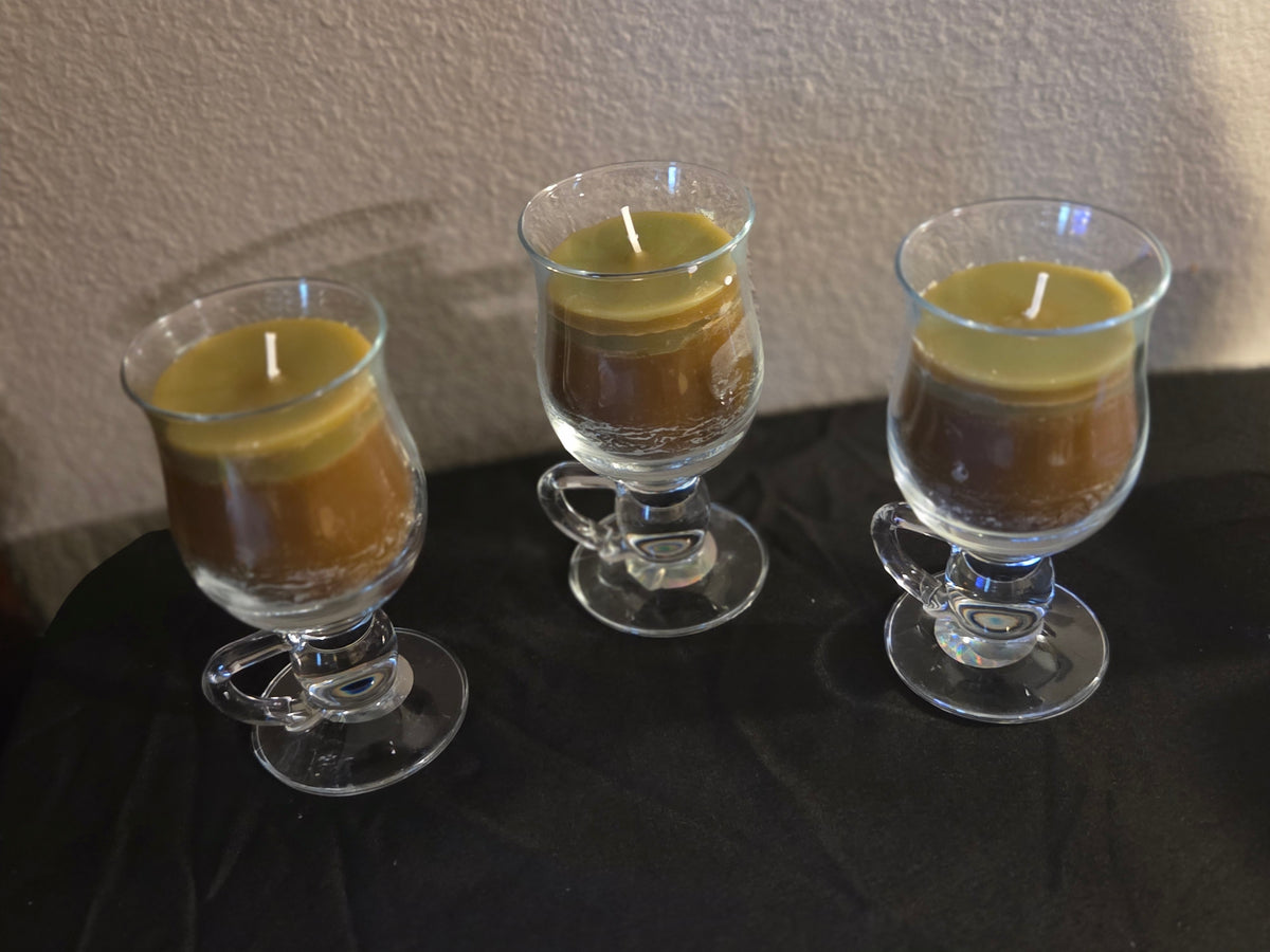 Three vanilla sage soy wax candles in clear footed glass mugs with curved handles.
