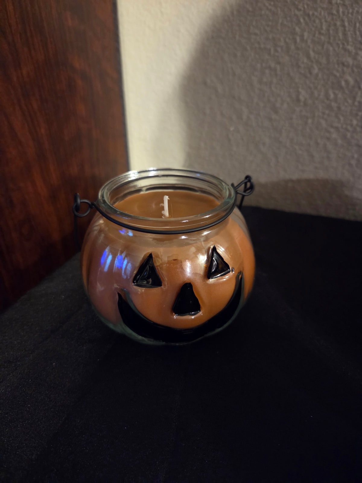 Pumpkin spice soy wax candle in a glass jack-o’-lantern jar with a black wire handle.